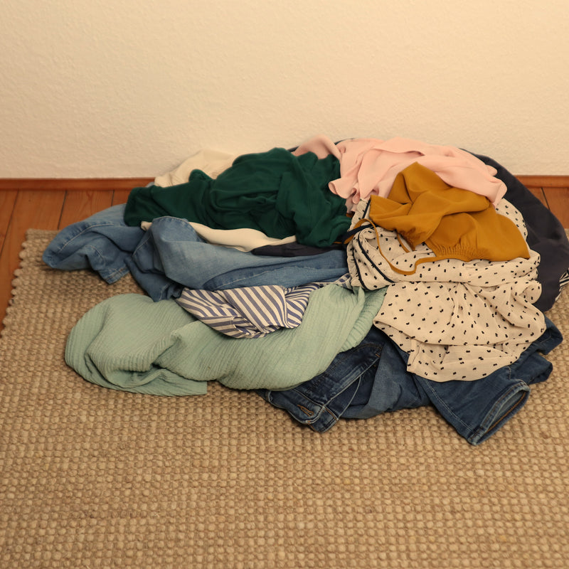 Kleiderhaufen auf einem Wollteppich als Symbol für Fast Fashion