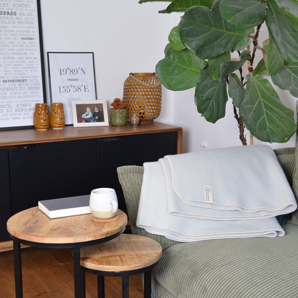 Bild mit einer Decke auf einem Sofa in wohnlicher Umgebung mit einem Couchtisch mit Teetasse und einem Buch