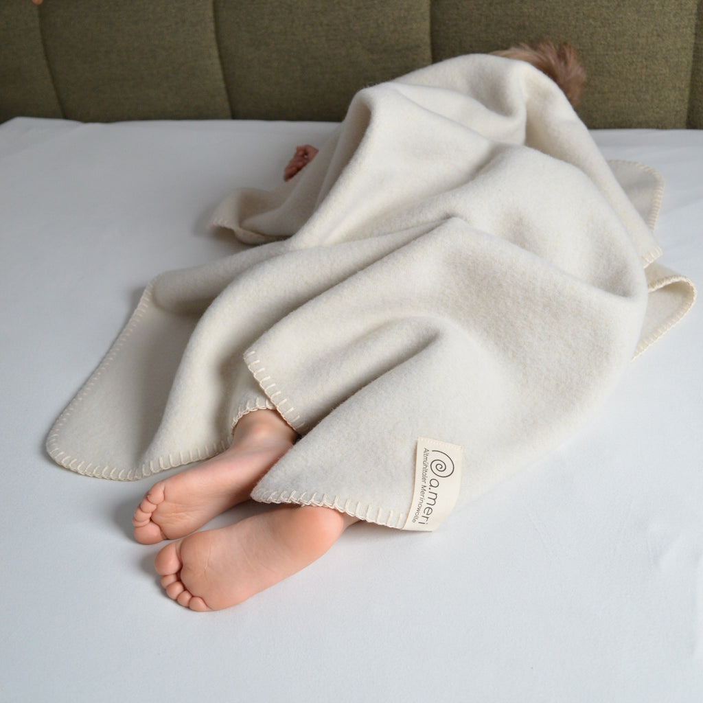Bild mit einem Kleinkind auf dem Bett liegend zugedeckt mit einer Decke Kinding. Füße schauen raus.
