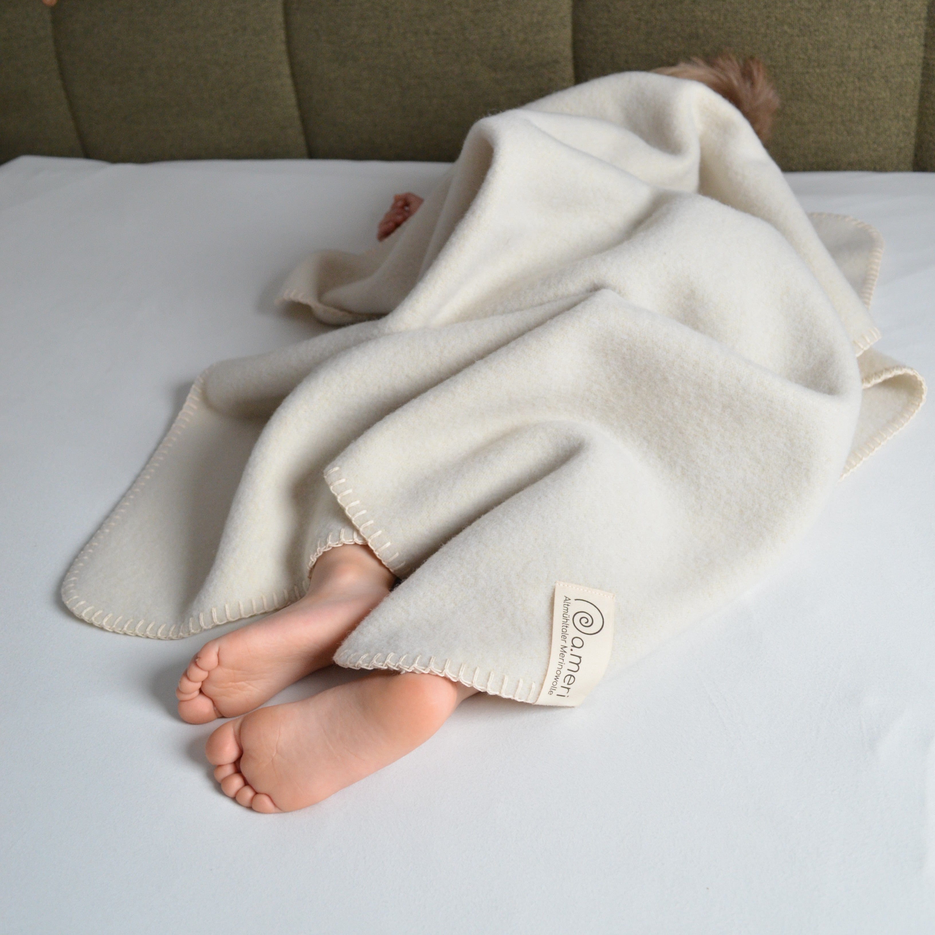 Bild mit einem Kleinkind auf dem Bett liegend zugedeckt mit einer Decke Kinding. Füße schauen raus.
