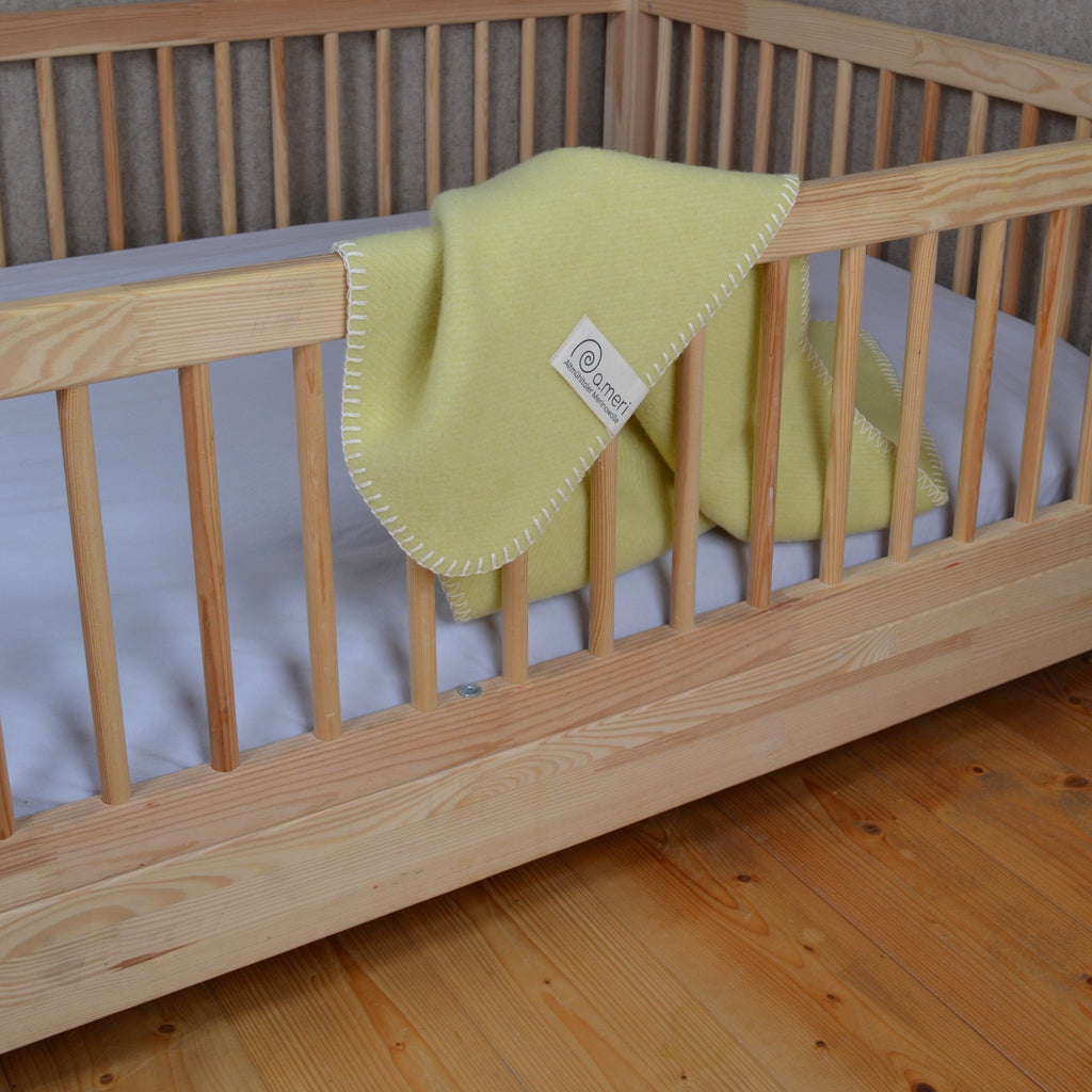 Bild mit der Decke Kinding in der Farbe Magerrasen. Decke hängt über das Gitter eines Kinder-Bodenbettes